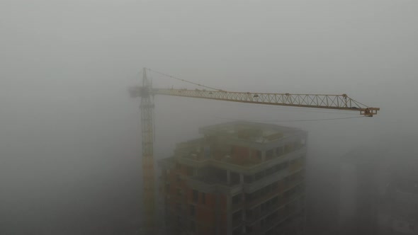Birds eye view on tower crane in fog standing next to residential building. alt