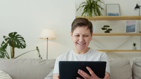 Smiling Elderly Mature Woman Resting on Sofa Using Digital Tablet Alone at Home alt