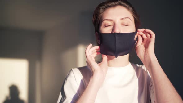 A Young Woman Puts on a Reusable Protective Mask at Home and Looks Into the Camera, Coronavirus 