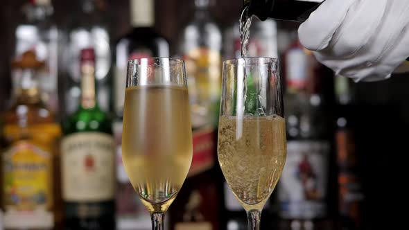 Closeup of a Waiter in Gloves Pouring Champagne Into Two Glasses at the Bar alt