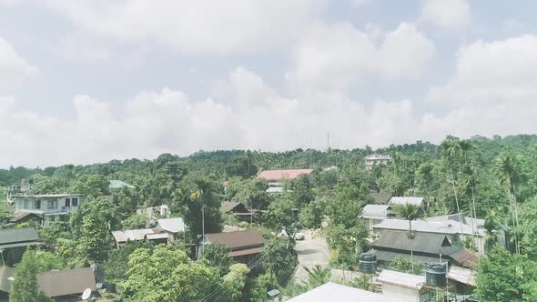 Cloudy sky over village with houses surrounded by tall trees of tropical forest alt