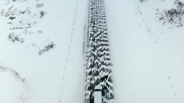 Aerial Tracking Tilt Reveal View of Van Car Driving Moving on a Snowy Road in Winter Through Wild Ar alt