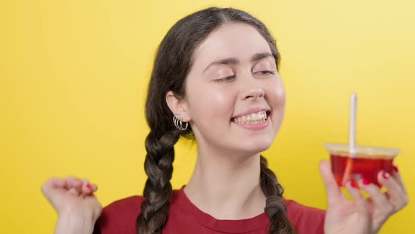 Portrait of a smiling girl holding a jar of jelly and sticking a spoon in it. Yellow background alt
