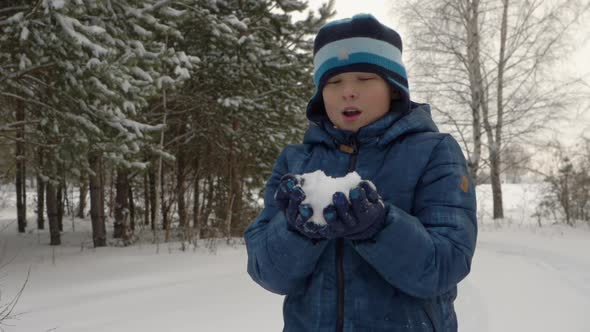Boy Teenager Blowing and Throwing Up Snow While Winter Walk in Snowy Forest alt