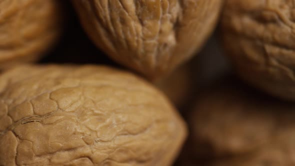 Cinematic, rotating shot of walnuts in their shells on a white surface  alt