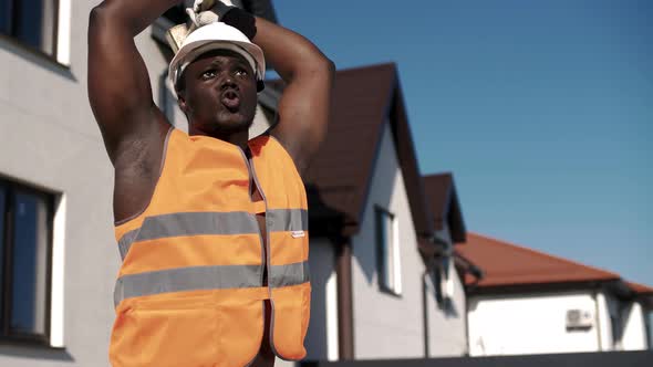 Muscular African American in uniform waving a sledgehammer at a construction site. alt