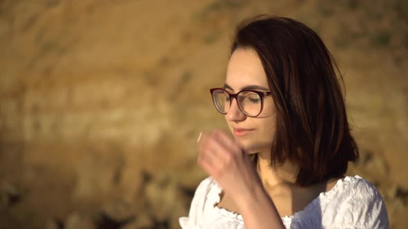 Attractive Young Woman on the Background of a Clay Rock. A Girl with Glasses Straightens Her Hair alt