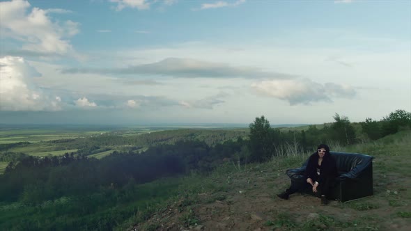 Joyful Guy Sings a Song Sitting on the Couch on a High Mountain Where you Can See the Clouds and the alt