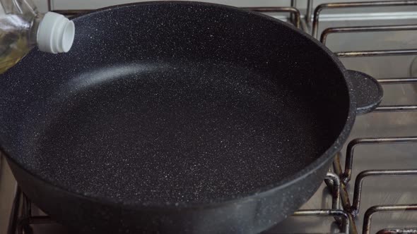 Cook pours sunflower oil into a frying pan. Kitchen pan stands on Stove alt
