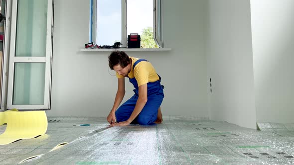 A Professional Master of Underfloor Heating Installation is Laying Out and Glue the Insulation for