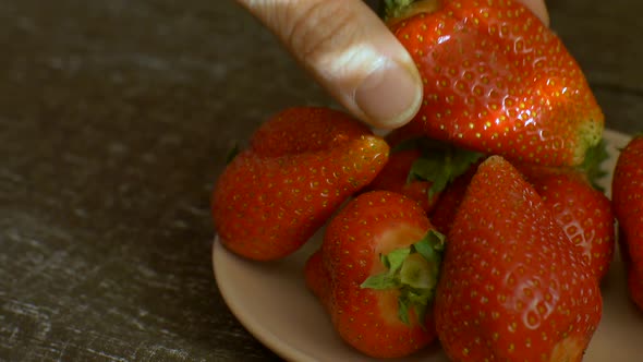 Woman's Hand is Putting the Strawberry to White Plate on Wooden Table alt