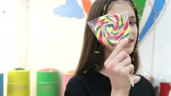 Smiling Teenage Girl in a Black Tshirt with a Lollipop on a White Background alt