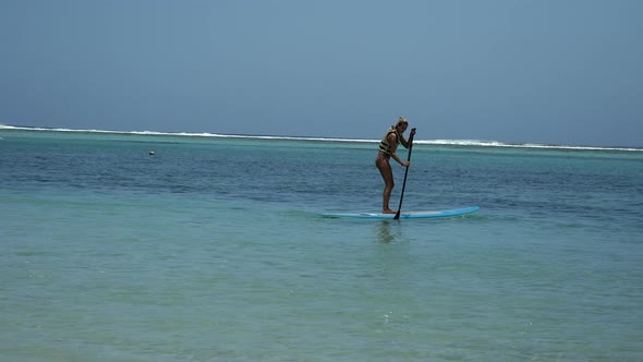 A Teenage Girl On Stand Up Paddle Board on crystal clear indian ocean in summer alt