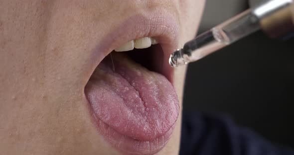 Woman Taking Medicine Cannabis Oil Drip Drops From a Pipette Into the Mouth alt