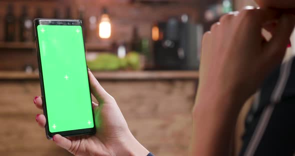 Woman Focused on Her Smartphone While Displaying a Green Screen alt