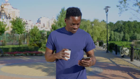 Happy African Adult Male Wears Blue Tshirt Looks at Navigation in Smartphone alt