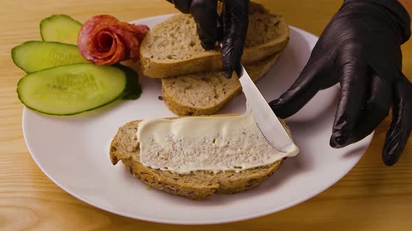 Hands in Black Gloves Smearing Knife on Soft Cheese or Butter on Fresh Slice of Bread Put Sausage alt