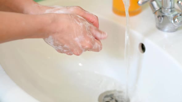 girl washes her hands with soap in the bathroom over the sink next to flowing water. alt