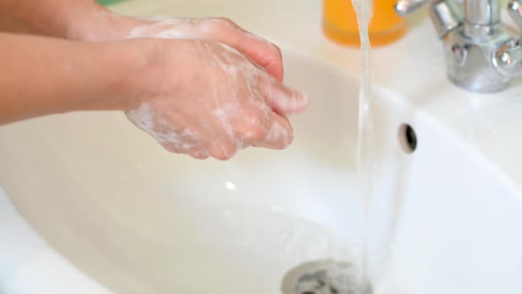 girl washes her hands with soap in the bathroom over the sink next to flowing water.