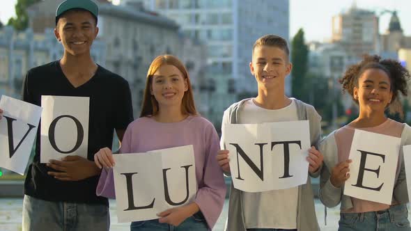 Group of Multiracial Teenagers Hold Volunteers Sign in Hands, Smiling on Camera alt