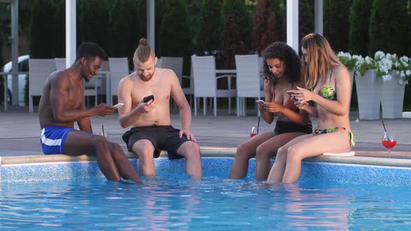 Joyful Friends Using Phones Sitting on Pool Side alt