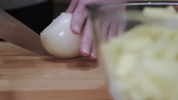 The chef's hand is cutting raw onion into slices with a knife on a cutting board.