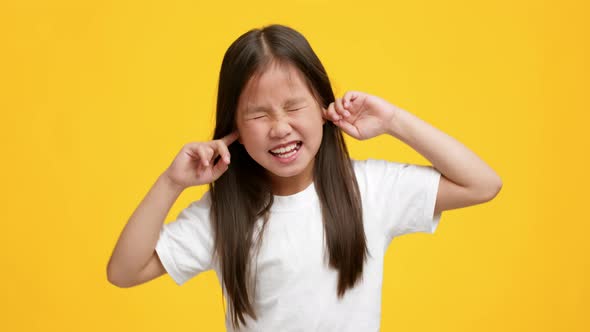 Naughty Little Asian Girl Plugging Ears With Fingers Yellow Background alt