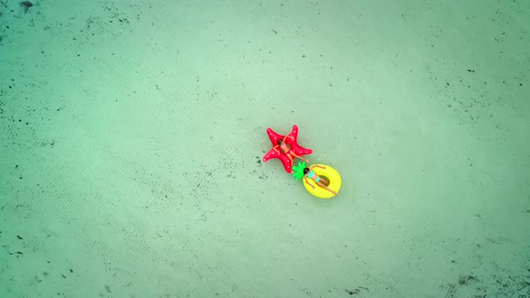 Aerial view of two girls floating on inflatable mattress in transparent sea, holding feet. alt
