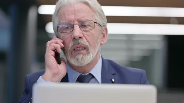 Close Up of Old Businessman with Laptop Attending Call on Phone alt