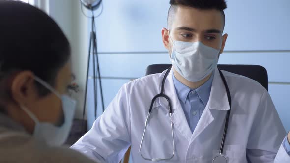 A Young Male Doctor in a Mask Talks to an Indian Patient Shows The Result of A Disease Test alt