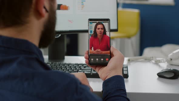Back View of Project Manager Holding Smartphone Listening Remote Leader alt