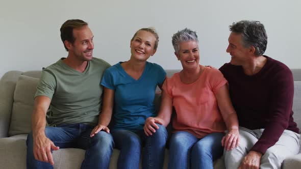 Happy caucasian couple and senior parents or in laws sitting on couch talking and smiling to camera alt
