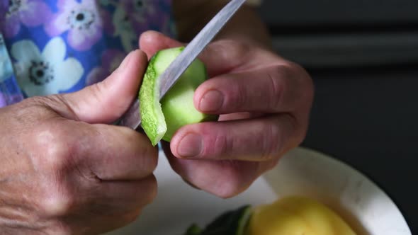 Closeup of peel and cut cucumber with knife in wrinkled hands