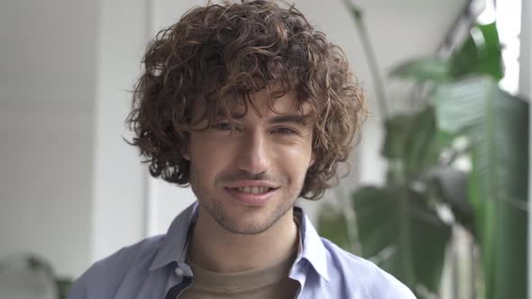 Portrait of Handsome Hispanic Man with Curly Hair Standing at Home Looking Happy to Camera with alt