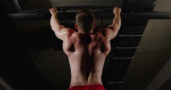 A man with beautiful muscles on his back, in the gym, pulls himself up on a horizontal bar alt