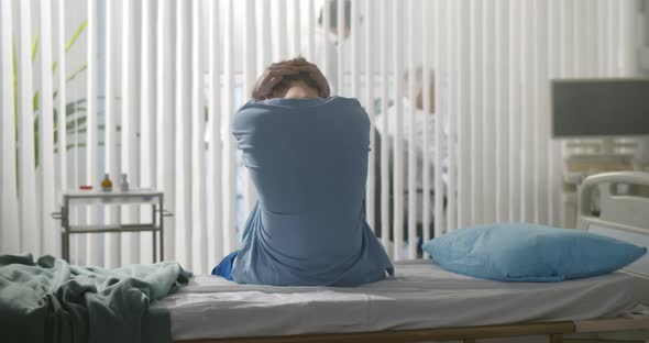Back View of Young Desperate Man Sitting at Hospital Bed Alone alt