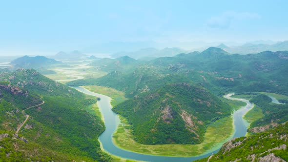 Blue Crnojevica River Flowing Curves Through Green Valley Toward Distant Mountains of Lake Skadar in alt