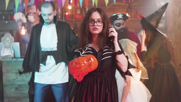 Young Attractive Girl in Witch Costume Dances with a Jack-o-lantern in Her Hands alt