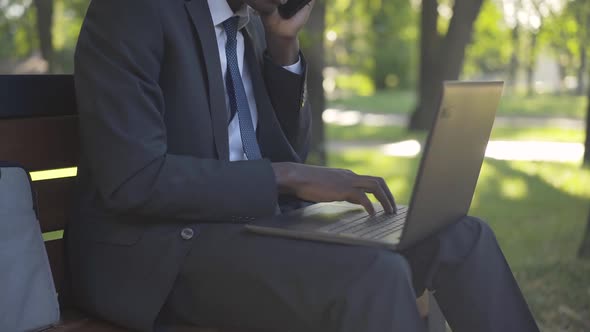 Unrecognizable African American Man Typing on Laptop Keyboard in Sunlight As Sitting on Bench in alt