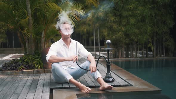 Young Caucasian Man Sits at the Poolside and Smoking Hookah in Slow Motion alt
