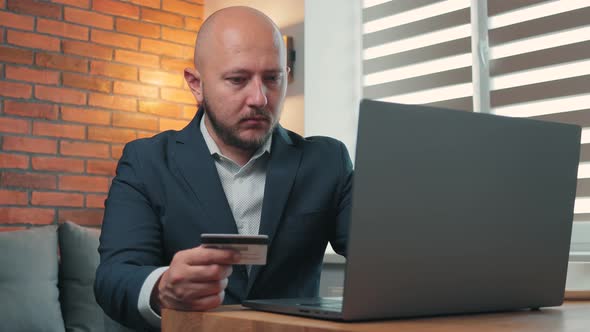 Young man in the suit holding a credit card and making online purchases through a laptop
