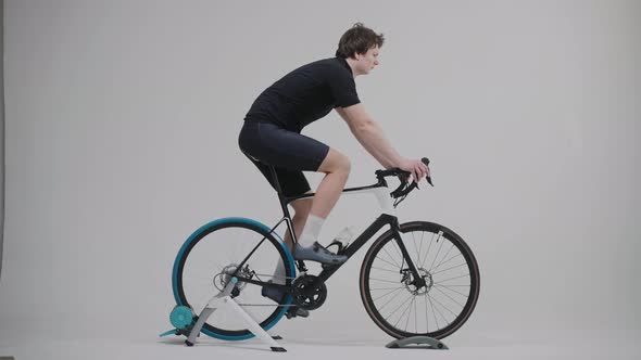 Side View of a Cyclist Training on an Exercise Bike in Bright White Studio