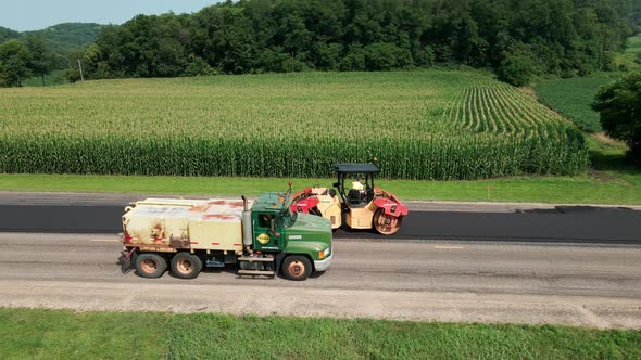 Aerial view of steamroller working to finish newly laid blacktop on rural highway in summer.