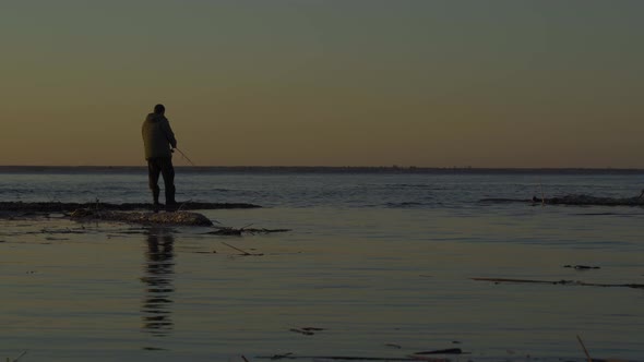 A Man Fisherman Catches Fish at Dawn on the Spit of a Large Reservoir. Fishing on the Volga River alt