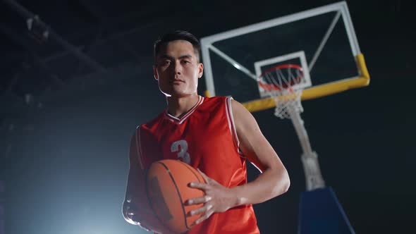 Portrait of an Asian Basketball Player Holding a Ball in Her Hands and Serious Looking at the Camera alt