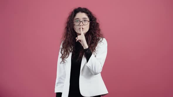 The Young Woman Balanced with Curly Hair Holding Her Finger to Her Lips Shows the Sign of Silence alt