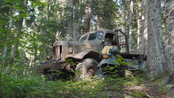 Female Traveler Examining Abandoned Vehicle In Forest