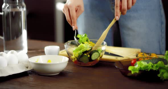 Women's Hands Mix Fresh Salad in a Bowl with a Spoon and a Spatula