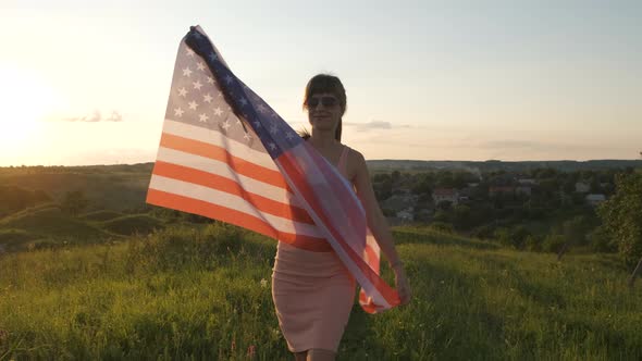 Young woman posing with USA national flag outdoors at sunset. Positive girl celebrating  alt