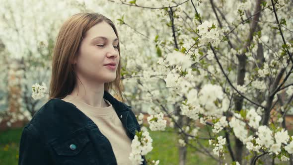 Beautiful young woman in a dark denim jacket in the spring garden in bloom alt